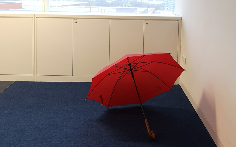 Red umbrella placed open on a blue carpeted floor inside a room with white cabinets