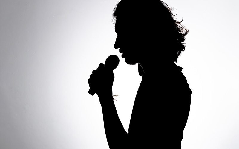 Silhouette of a person singing into a microphone against a bright white background