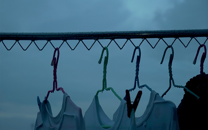 White clothes hanging on colorful plastic hangers outdoors on a metal rack in dim, cloudy weather
